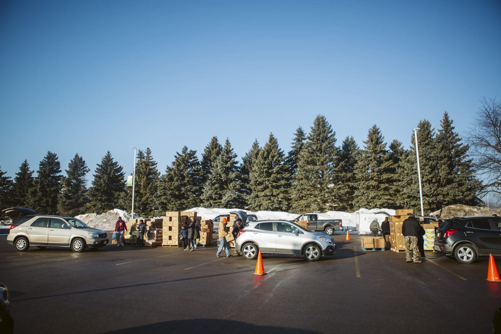 A group of individuals gathered in a parking lot, surrounded by various cars.