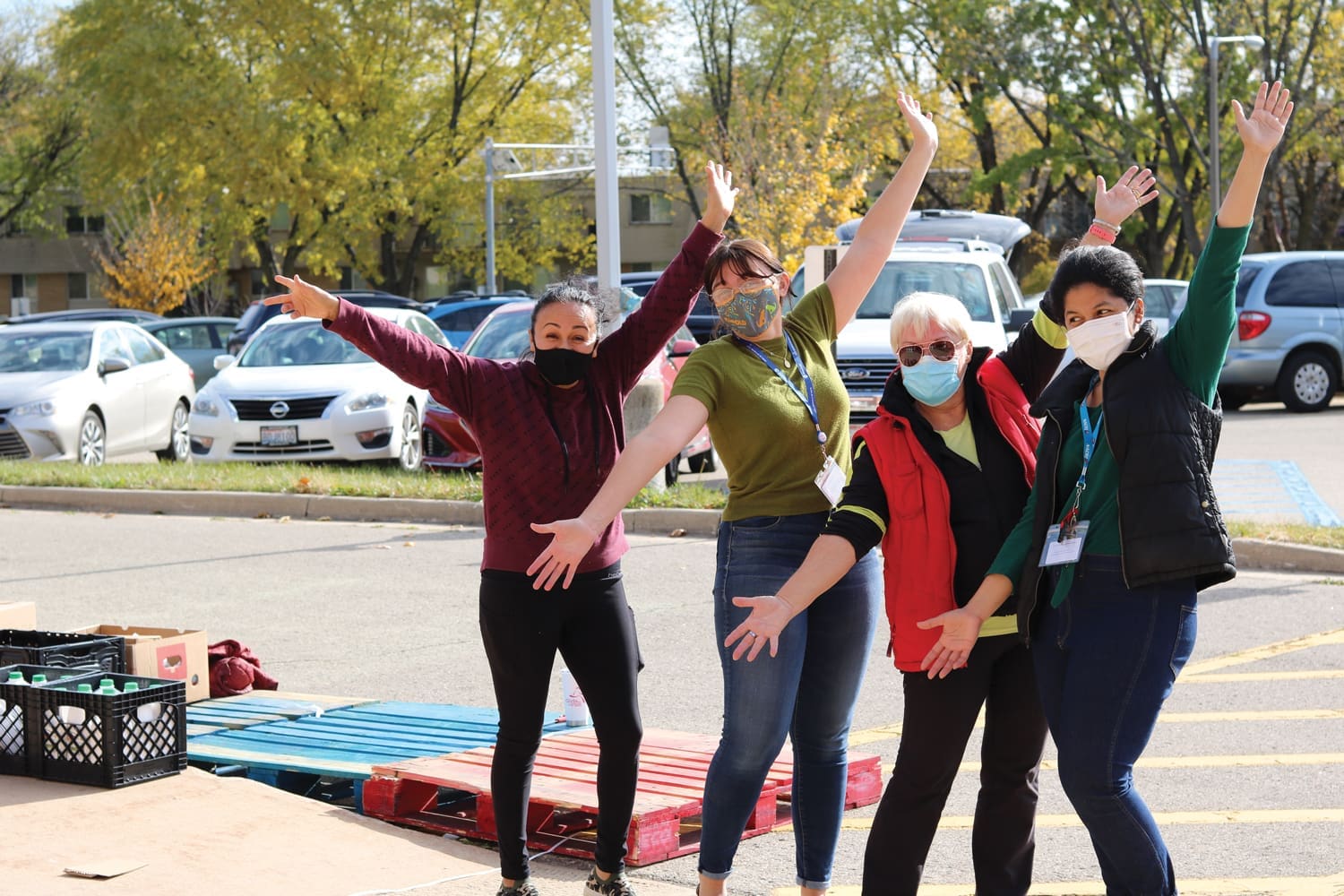 4 volunteers at elementary school arms up celebrating the end of a mobile distribution Early fall sunny green trees