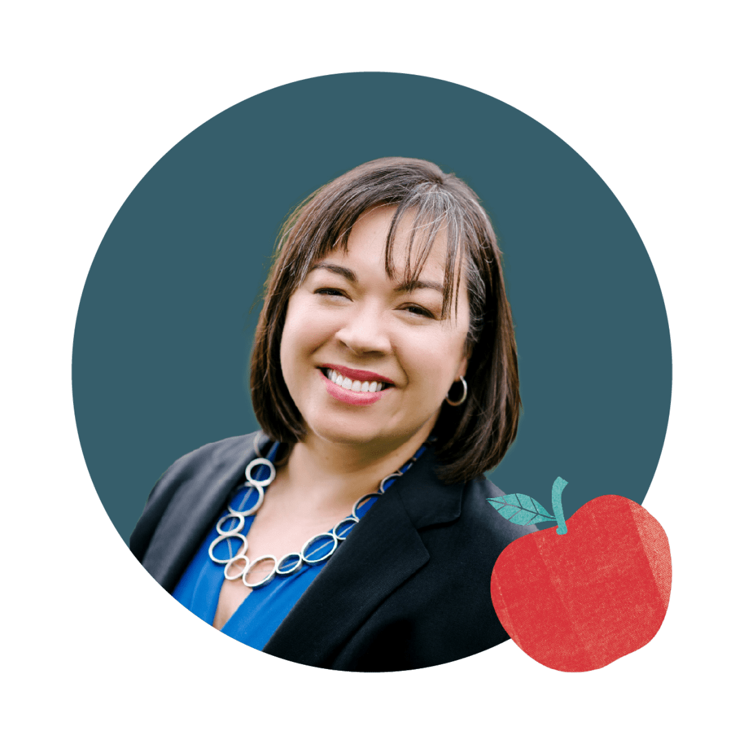Smiling woman in a blue blouse and black blazer wearing a circular teal background with an apple illustration in the corner